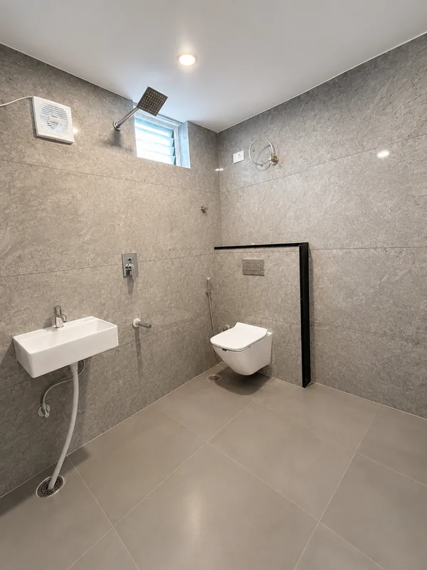 Bathroom of the model flat, tiled to the ceiling in grey stone-effect tile with a wall-hung WC and rain shower